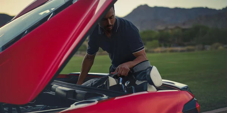 A photo of a man loading golf clubs in the back of a Chevy Corvette.
