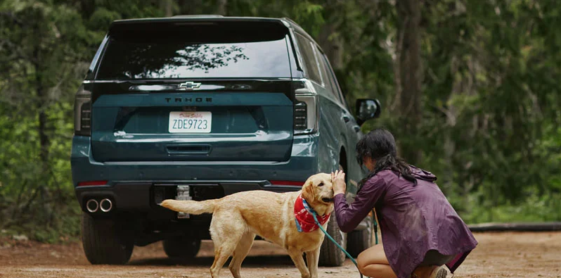 Photo of a woman and her dog behind a parked 2026 Chevy Tahoe.