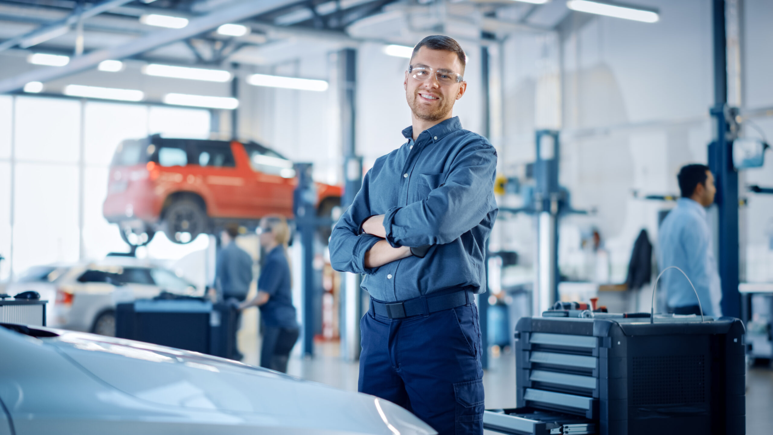 A photo of a car mechanic standing in a auto repair shop.