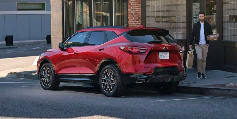 A photo of a man walking toward the back of a red 2025 Chevrolet Blazer to load bags in the back.