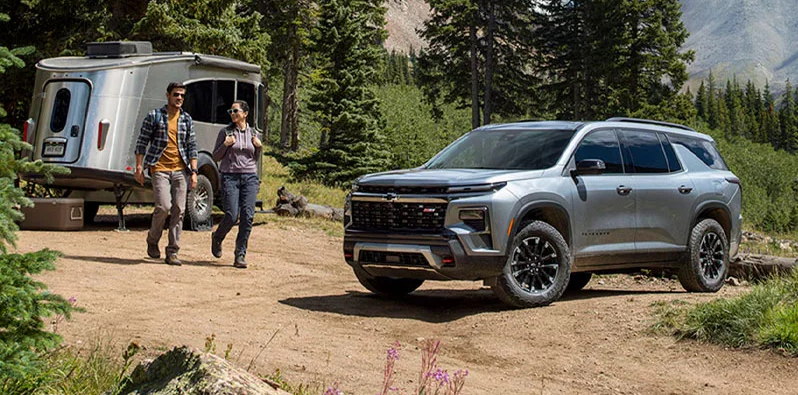 A man and woman walking from a camper toward a 2026 Chevrolet Traverse.